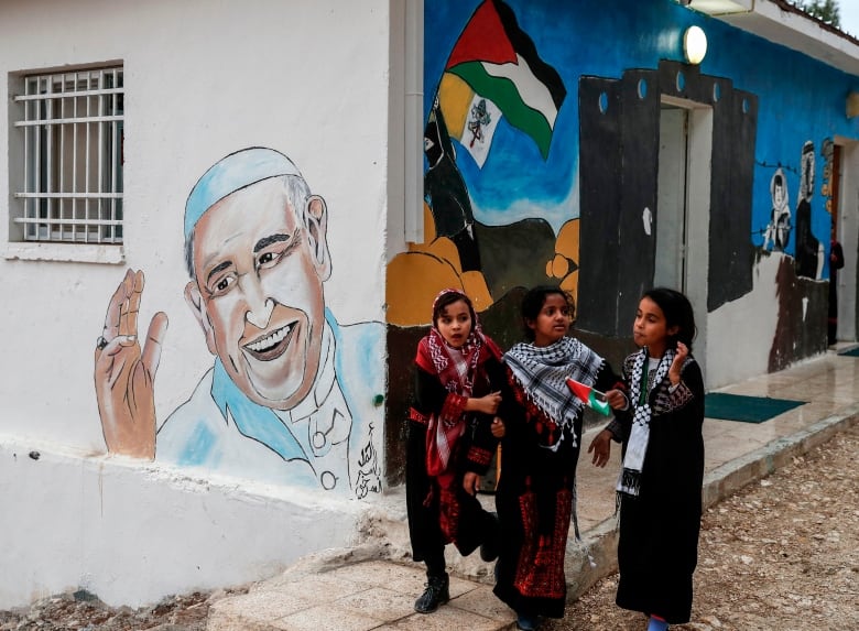 Girls walk past a mural of the Pope.