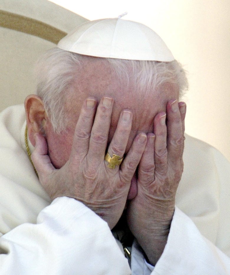 A man in white robes prays with his hands covering his head.