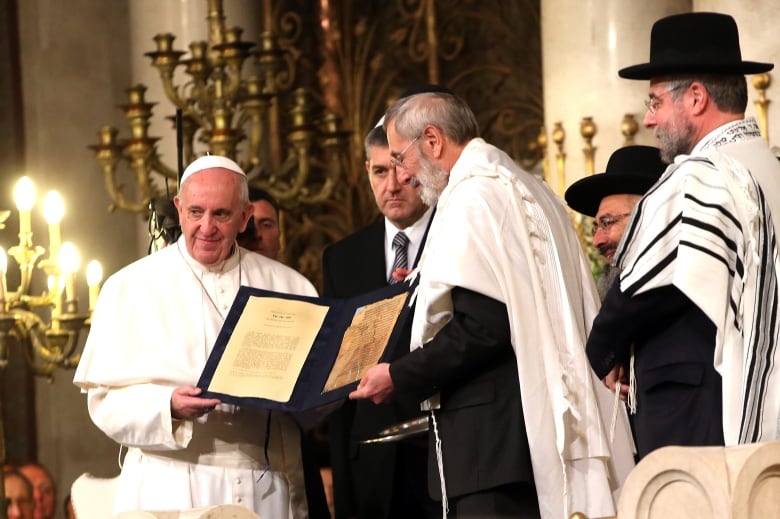 Men stand together holding a file with two pages on it.