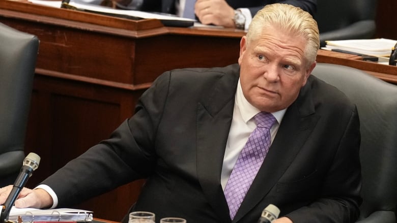 A bald man wearing a black suit looks away from the camera