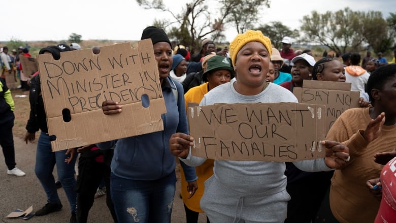 Women march outside holding handwritten signs on carboard that read 'We want our famalies!!' and 'Down with minister in presidency'