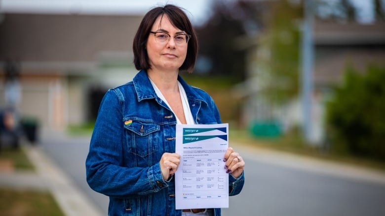 Woman standing, holding paper, looking at camera. 