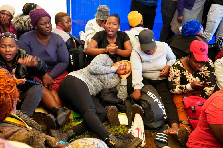 A large group of people, mostly women, huddled together on the ground