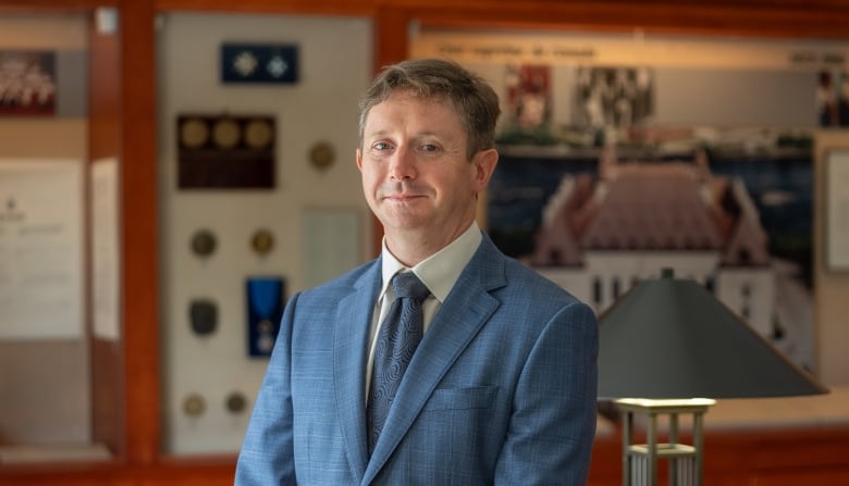 Man standing in an office, smirking, looking at camera. 