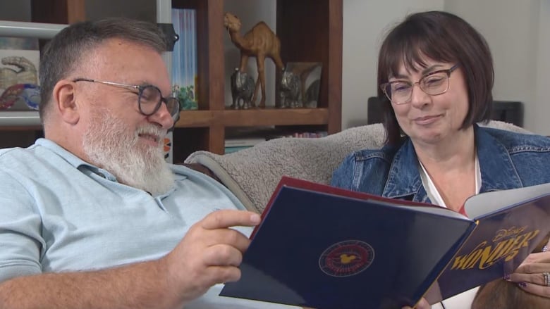 A man and a woman seated on a couch looking at a photobook. 