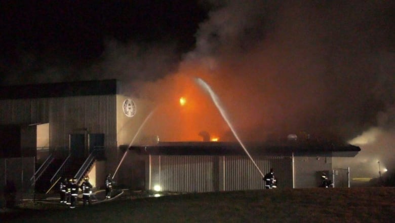 Multiple firefighters spray water from their fire hoses on a fire at a school in the middle of the night.