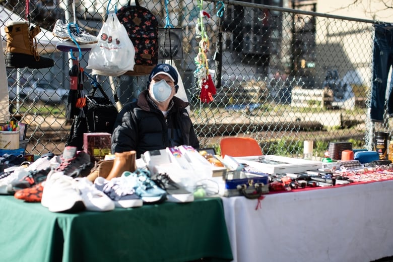 A man wearing a mask at a vendors' stall outdoors sells goods.