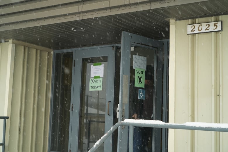 Two people open a door as snow blows around them.