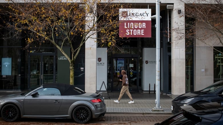 A man walks by a store that says Legacy Liquor Store on a sign affixed to a pole in front of it.