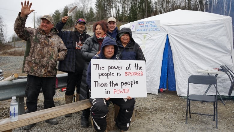 People smiling, waiving signs. Behind them is a large tent.