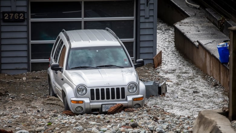 A car in a sloped driveway is surrounded by mud and debris.