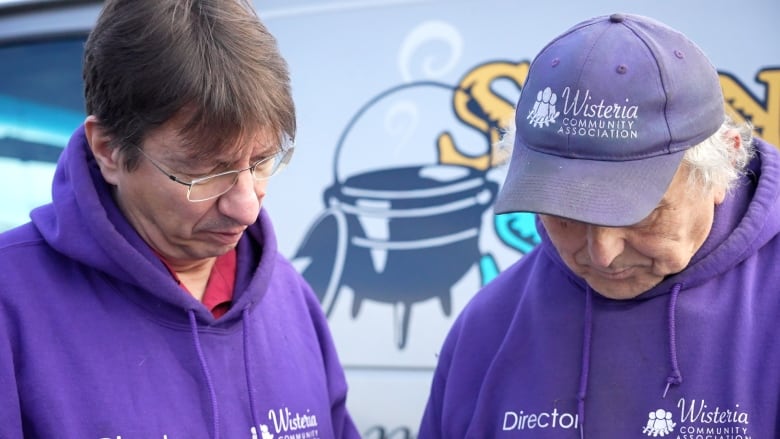 Two men wearing purple hoodies look down.