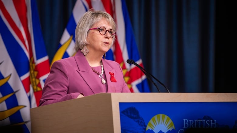 A woman in glasses and a pink outfit speaks from a podium that says 'British Columbia' on it.