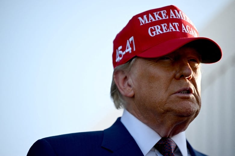 A man in a suit and bright red hat is pictured. The ballcap says 