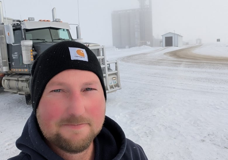 A man stands in the snow near his truck.