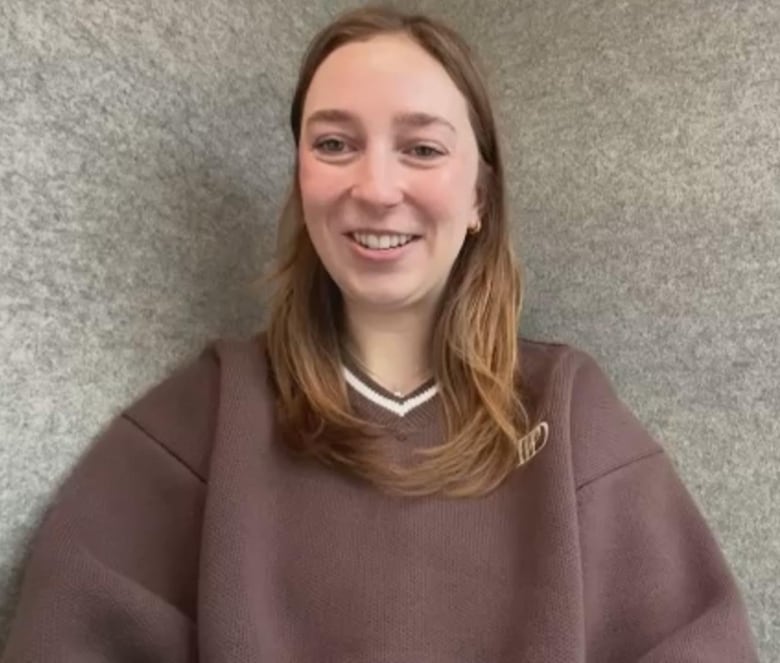 A young woman in a large brown sweater smiles in a Zoom window.