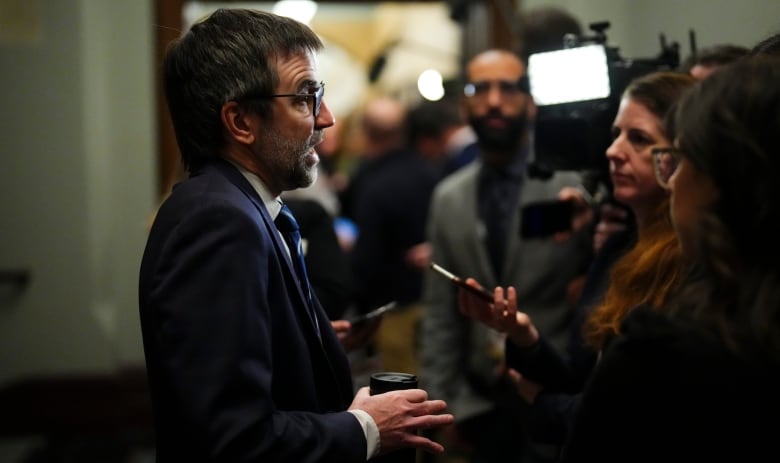 A man stands in front of a group of reporters.