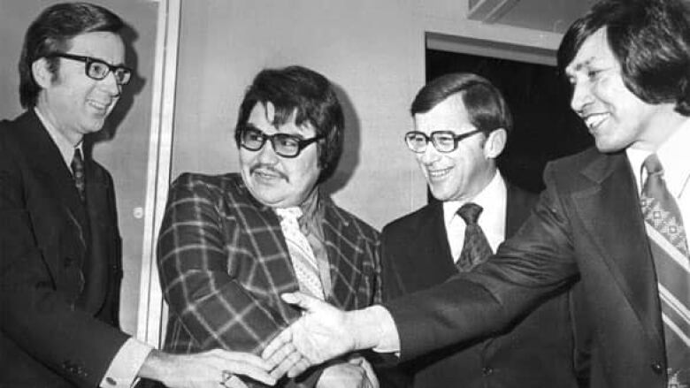 A black and white photo of four men in suits shaking hands.